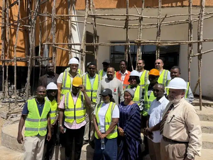 Group of construction workers in high-visibility vests and hard hats posing in front of a building under wooden scaffolding at a construction site.