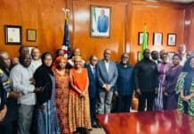 Foreign Minister Calls for Stronger Diaspora Partnership, Improved Consular Services in US Group of people in formal and traditional clothing posing in a wood-paneled room with flags behind them.