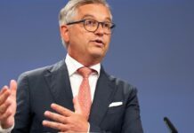 EU Commissioner Counters Dutch Minister’s Claim, Cites Technical Reasons for Sierra Leone Funding Hold Man in a dark suit and pink tie giving a speech, gesturing with his hands.