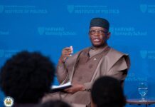 President Bio Tells Harvard: Africa Must Put African Interests First in Global Partnerships African man in traditional brown attire, speaking with a microphone against a blue Harvard Kennedy School Institute of Politics backdrop, audience in foreground