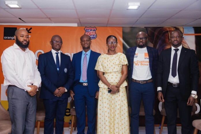 Six professionals in formal attire posing for a group photo at a corporate event, with an orange branded backdrop behind them.
