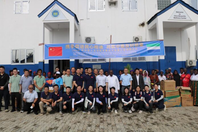 Group of Chinese and African participants posing in front of a white building with a blue banner about China–Africa friendship, and stacked donation boxes nearby.