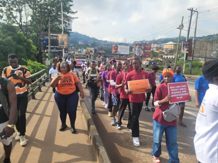 A diverse group of people marching across a bridge in a street protest, holding signs and banners.