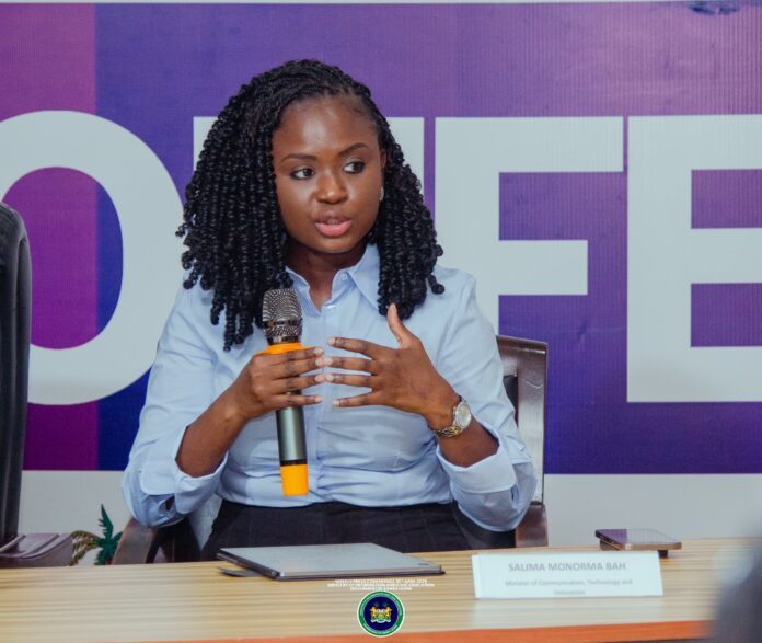 Woman with braided hair speaks into a microphone at a panel, purple backdrop, nameplate reads Salima Monorma Bah on the desk.