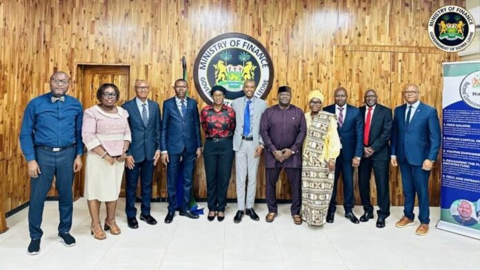 Ten professionals in business attire posing for a group photo in a Ministry of Finance room with a seal on a wood-paneled wall in the background.