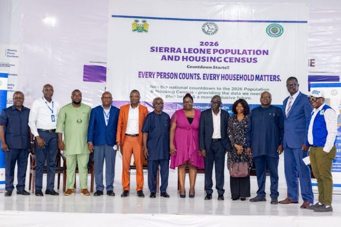 Group of men and women in formal attire standing on a stage in front of a banner that reads '2026 Sierra Leone Population and Housing Census' and 'Every person counts, every household matters.'