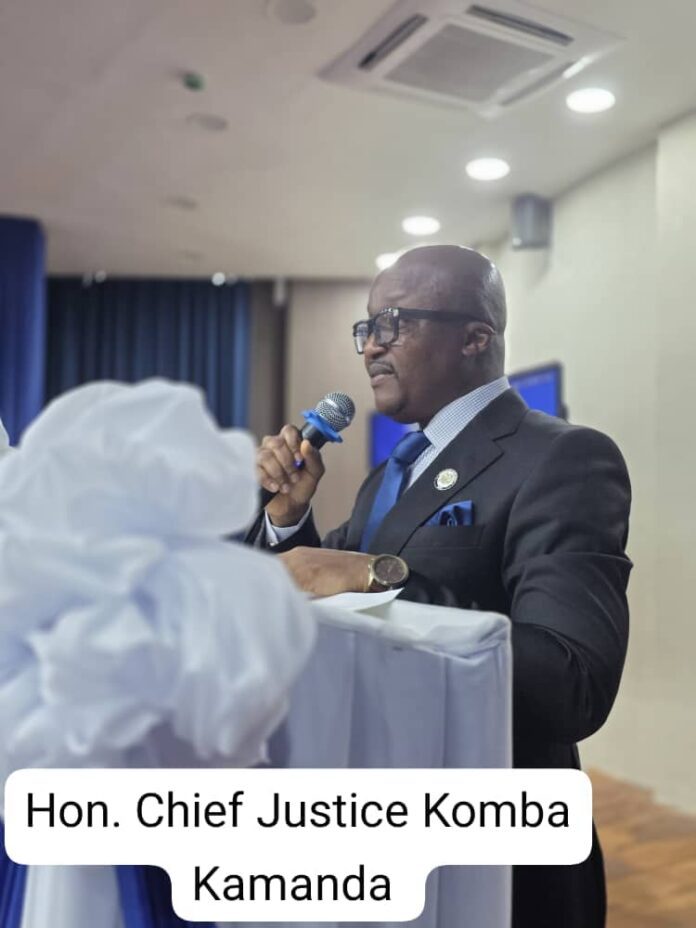 Hon. Chief Justice Kamanda delivering a speech at a podium in a suit, microphone in hand.