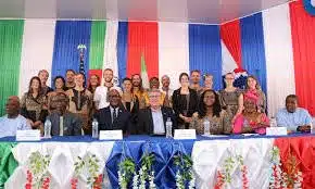 Group photo of officials and delegates at a formal ceremony, seated at a decorated table with a red, white, and blue backdrop behind them.