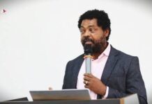 AWOL Chairman Ahmed Sahid Nasralla Urges Government to Declare Mental Health a National Health Emergency Man in a pink shirt and dark blazer speaks into a microphone at a podium during a talk or event, with a small logo visible in the corner.