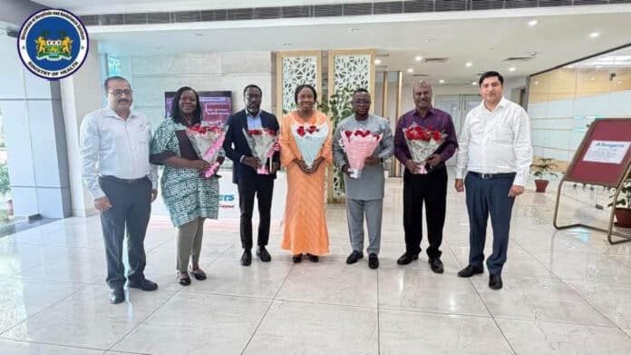 Seven people stand in a bright lobby, each holding flower bouquets; Ministry of Health logo is visible in the top-left corner.
