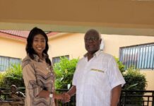 Former President Koroma Throws Weight Behind National Unity Conference, Calls for Trust & Political Cohesion Two adults shake hands on a tiled outdoor patio; woman in a beige patterned dress and brown heels, man in a white short-sleeve shirt and dark pants, smiling at the camera.