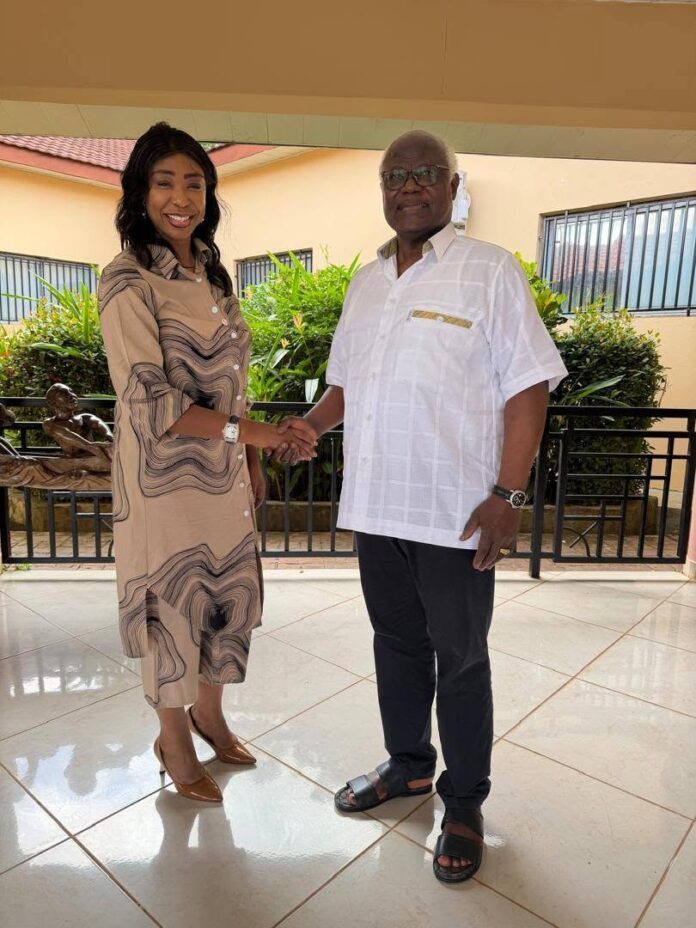 Two adults shake hands on a tiled outdoor patio; woman in a beige patterned dress and brown heels, man in a white short-sleeve shirt and dark pants, smiling at the camera.