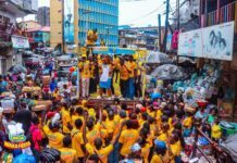 Onga Marks World Food Day 2026 with Three-Day Waka Fiesta Roadshow Crowd in a busy market street cheering at a yellow-clad parade with a cartoon mascot on a float.