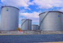 NP (SL) Strengthens Fuel Quality Assurance Through Routine Tank Cleaning and Inspection Three large silver storage tanks with external staircases at an industrial facility, blue sky above and a safety sign on the concrete wall in front.