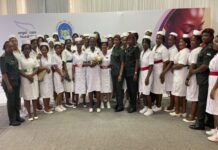 Angel Care Foundation Launches Blanket Initiative in Sierra Leone, Distributes 500 Blankets to Four Hospitals Group of women in white dresses with red sashes and a few in green uniforms posing for a photo at a health event with Angel Care Foundation branding in the background.