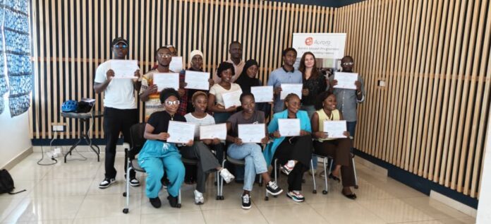 Group of diverse people posing with certificates after completing a program in a room with wooden slat walls.