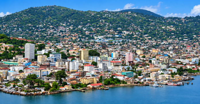 Coastal city with a densely built waterfront and green hills in the background under a blue sky.