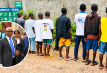 Chief Justice Reviews Magistrates’ Court Sentences, Orders Release of 11 Inmates at Kailahun Correctional Centre A line of young men standing with their backs to the camera in a dusty outdoor area beside a wall, with a blue 'Prohibited Items' sign; a circular inset shows formally dressed officials in a suit and sunglasses.