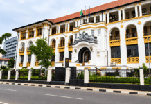 34-Year-Old Security Guard Pleads Guilty to CCTV Camera Theft, Bags Six-Month Jail Term Colonial-style white building with yellow trim, arched balconies, and a decorative arched entrance behind a black fence along a tree-lined street with flags on top.