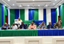 ECSL Validates 2025–2029 Strategic Plan in Makeni, Pledges Transparency and Stakeholder Ownership Panel of men seated at a long table during a formal meeting, with green and blue drapes in a decorated hall and water bottles on the table.