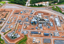 SLCAA Steps Up Drone Safety Oversight with Inspection at FG Gold Mine Aerial view of a large industrial site under construction, with roads, storage tanks, buildings, and heavy machinery scattered across reddish earth.