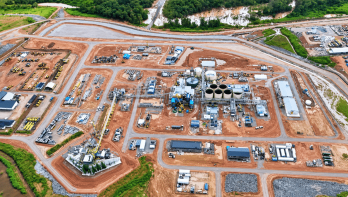 Aerial view of a large industrial site under construction, with roads, storage tanks, buildings, and heavy machinery scattered across reddish earth.