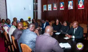Group of diverse officials seated around a long conference table in a formal meeting room, some taking notes; framed portraits line the wooden wall, with the Judiciary of Sierra Leone seal visible in the bottom right.