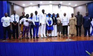 | The Calabash Newspaper Group of people standing on a stage for a formal event, blue curtains and a wooden floor visible behind them.