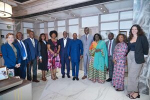 | The Calabash Newspaper Group of professionals in formal attire posing for a photo in a bright marble-floored office lobby or reception area.