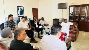 | The Calabash Newspaper A group of men sit in a semi-circle in an office meeting room, discussing around a coffee table with water bottles and documents nearby.