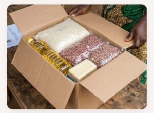 Open cardboard box with cooking supplies—oil, rice, beans—and a bar of soap, held by a person.