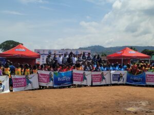 Large group of people standing behind banners at an outdoor sports event, with red sponsor tents and a clear blue sky above.