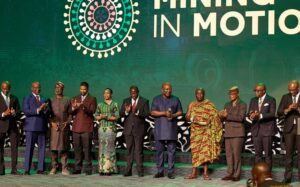 | The Calabash Newspaper Group of formally dressed people on a stage at a mining conference, clapping, with a green backdrop that reads 'MINING IN MOTION'.