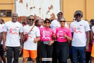 Group of diverse volunteers at a breast cancer awareness event, wearing pink and white shirts with ribbon logos and posing for a photo outdoors.