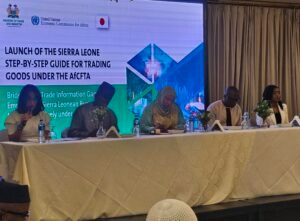 Panel of speakers at a conference with a large banner reading 'Launch of the Sierra Leone Step-by-Step Guide for Trading Goods under the AfCFTA' in the background.