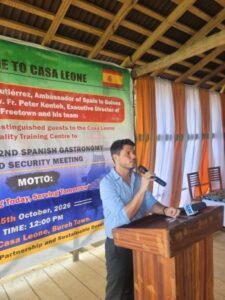Man in a blue shirt speaks into a microphone at a wooden podium, with a large Casa Leone banner in the background.