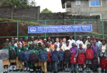 CRSG Strengthens Community Ties with Education Support for Mongegba Pupils Group of students and adults posing outdoors with backpacks, in front of a banner about a Sierra Leone donation project in progress.