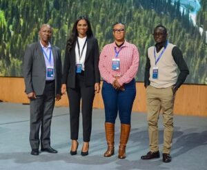 Four professionals stand together on a stage, posing for a group photo at a conference with lanyards and badges visible.