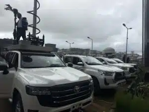 Technician in uniform standing on a raised platform on a service vehicle, working on telecom equipment mounted on a tall pole against a cloudy sky.