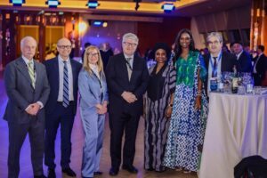 | The Calabash Newspaper Group of professionally dressed people posing together at a formal networking event near a high table with drinks and bottles in a dimly lit venue.