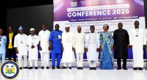 Group of officials standing on stage in front of a purple conference banner reading 'Conference 2026' and 'National Unity and Social Cohesion'.