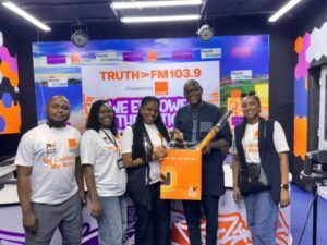 | The Calabash Newspaper Five people stand in a radio studio in front of a TruthFM103.9 backdrop, smiling and holding an orange branded bag.